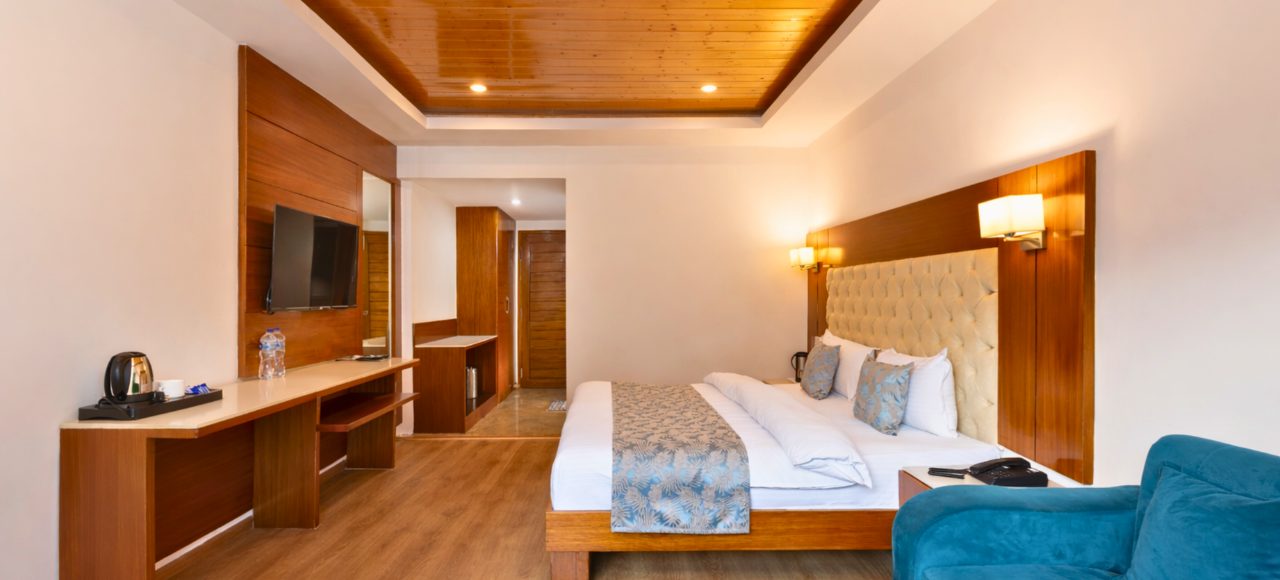 Hotel room with a king bed, tufted headboard, two bedside lamps, and a blue patterned runner.