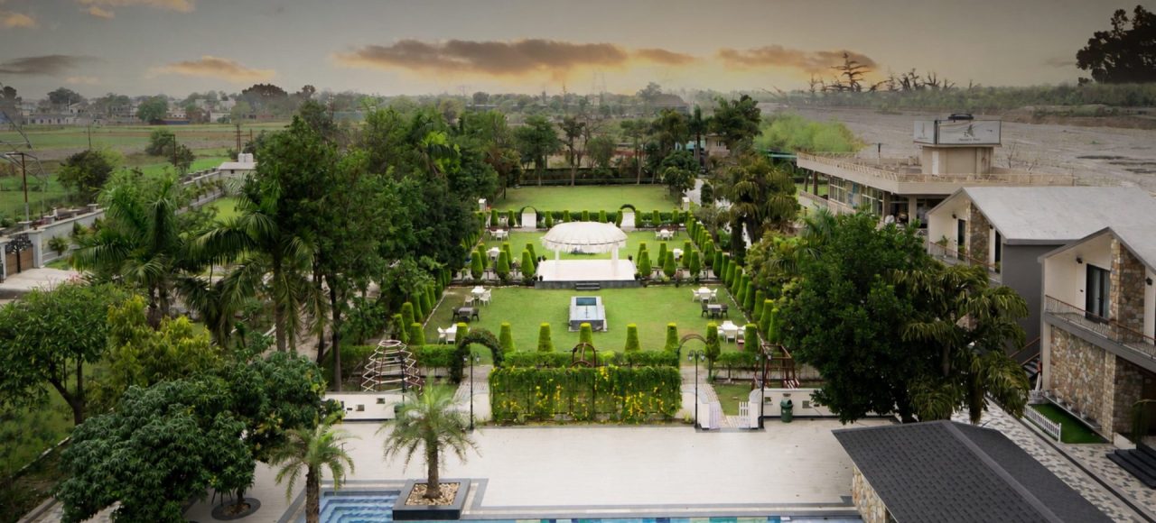 Aerial view of a resort with a rectangular pool, manicured gardens, and a central gazebo surrounded by chairs and paths.