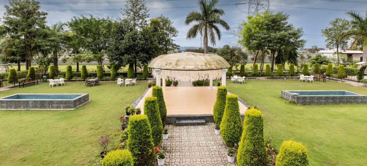 Formal garden with a central beige domed gazebo, stone path, and trimmed hedges surrounding a sunny lawn.