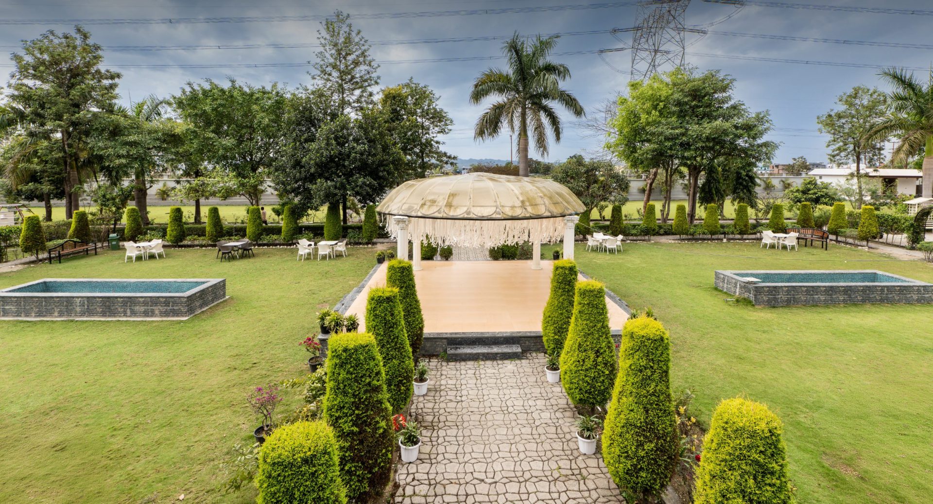Formal garden with a central beige domed gazebo, stone path, and trimmed hedges surrounding a sunny lawn.
