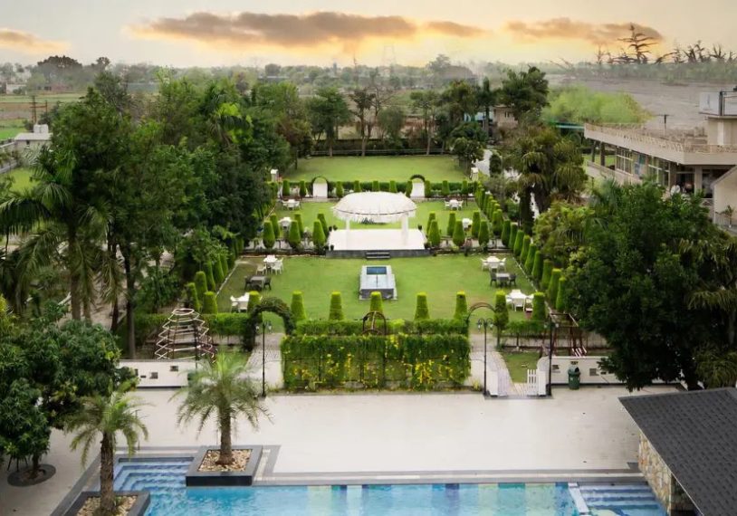 A landscaped hotel garden with a central lawn, white gazebo, and hedged paths surrounding a swimming pool in the foreground.
