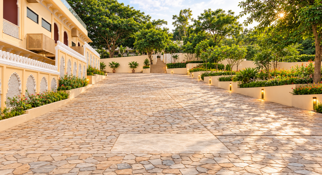 jüSTa Luxé – Monsoon Palace, Udaipur Sunlit stone walkway flanked by a yellow building on the left and terraced gardens on the right with trees overhead.