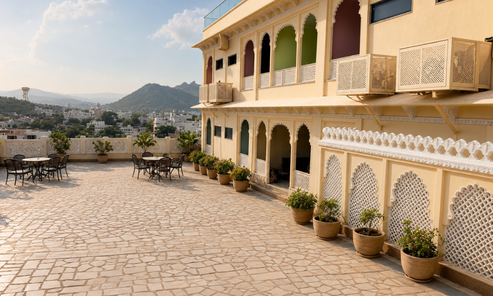 Rooftop terrace with arches on a beige building, potted plants, and several tables and chairs overlooking a townscape.