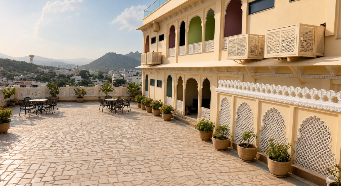 jüSTa Luxé – Monsoon Palace, Udaipur Rooftop terrace with arches on a beige building, potted plants, and several tables and chairs overlooking a townscape.