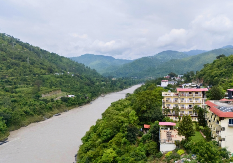 River winds through a green valley with forested hills; a cluster of buildings sits on the right hillside.